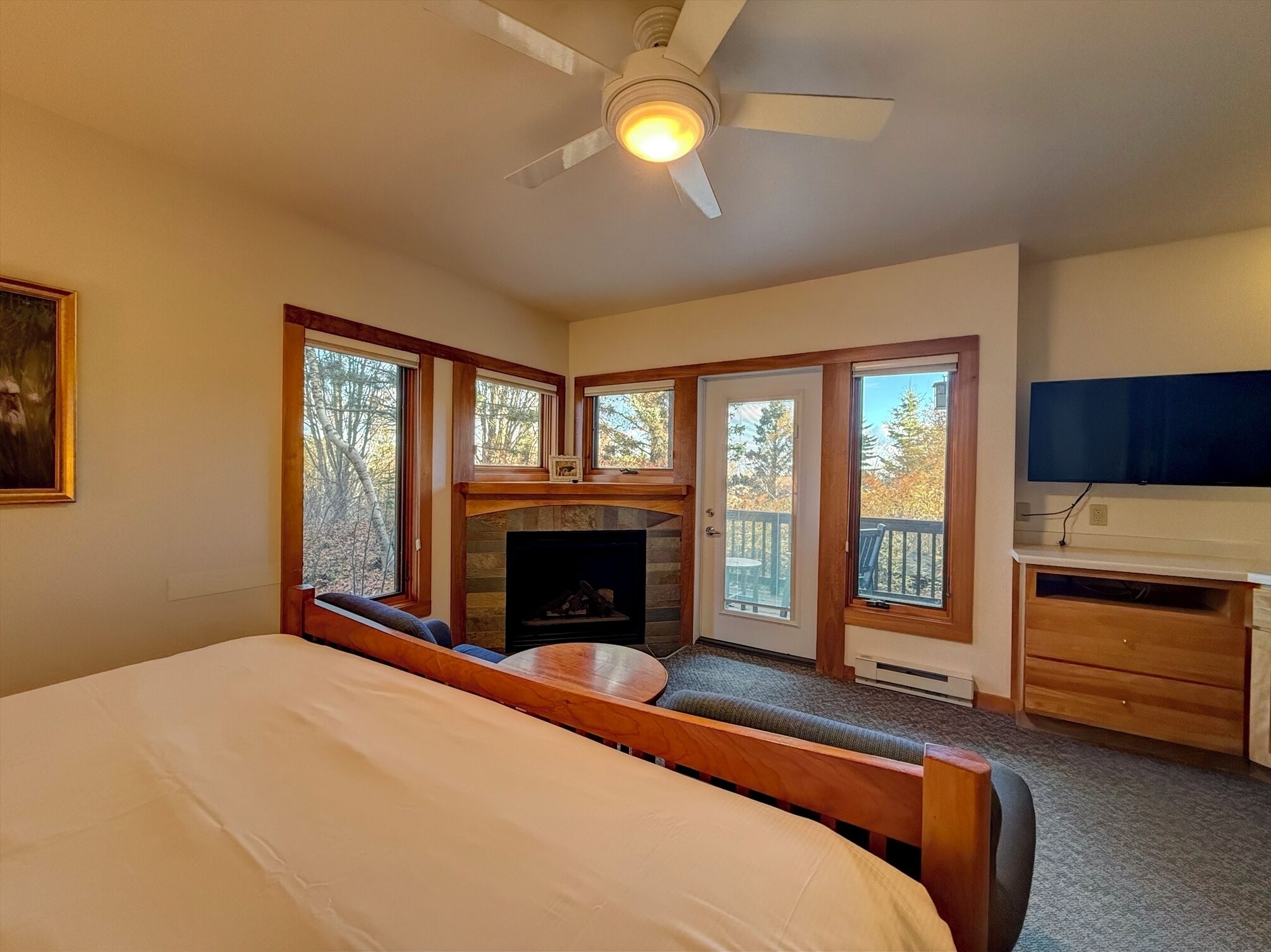 A bedroom with a bed, a fireplace, a desk, and large windows.