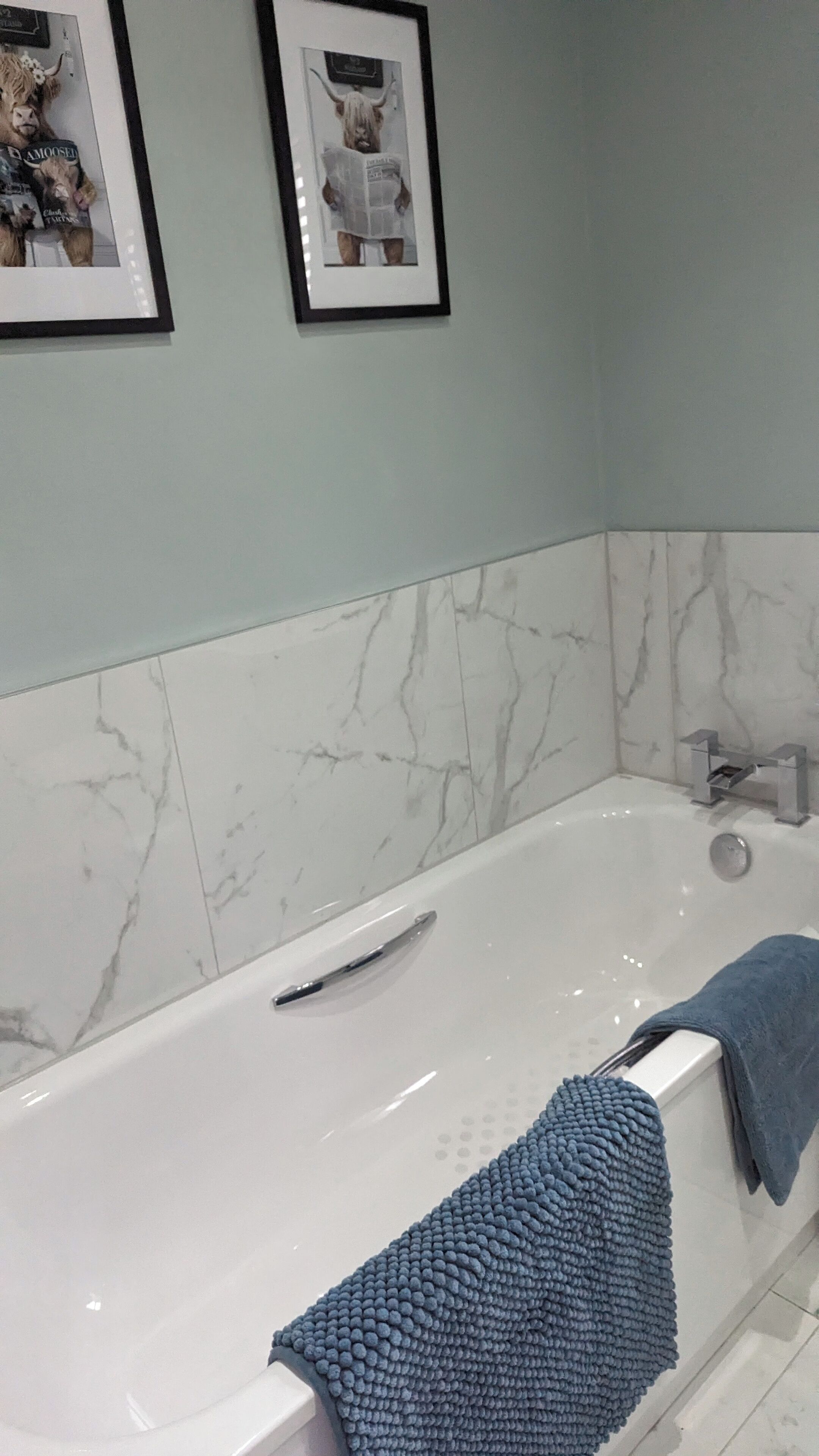 A bathroom with a white bathtub, marble walls, and a towel rack.