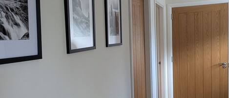 A hallway with framed pictures on the wall, a radiator, and a wooden door at the end.