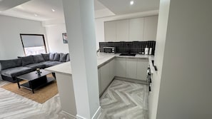 Una sala de estar moderna con un sofá gris, una mesa de centro y una cocina con microondas, armarios y suelo con motivo de espiga.