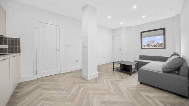 Un apartamento moderno con cocina, un sofá gris, una mesita y vistas a la ciudad a través de un ventanal.