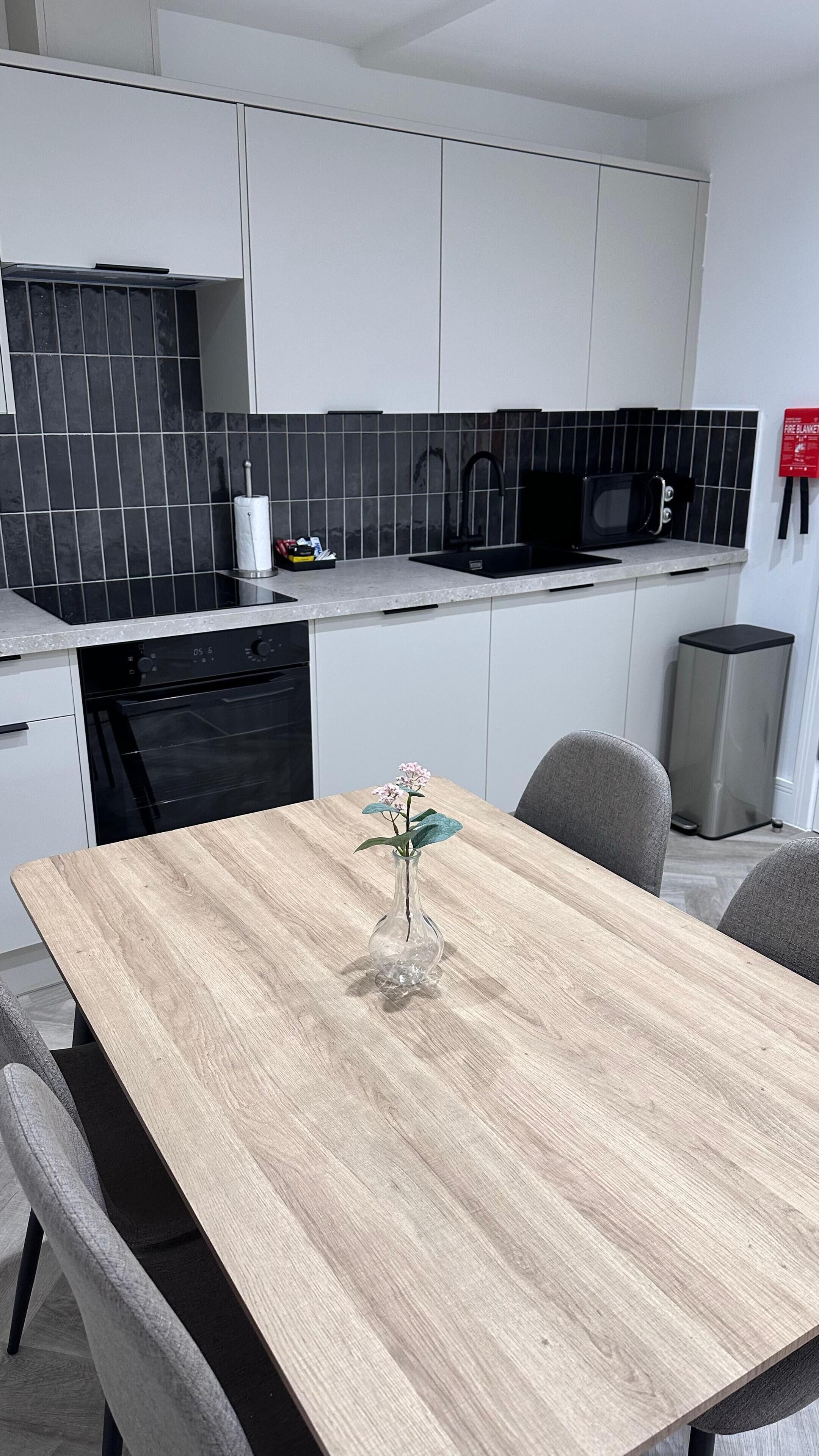 Ett modernt kök med vita skåp, svart kakel ovanför arbetsbänken, en mikrovågsugn och en papperskorg.