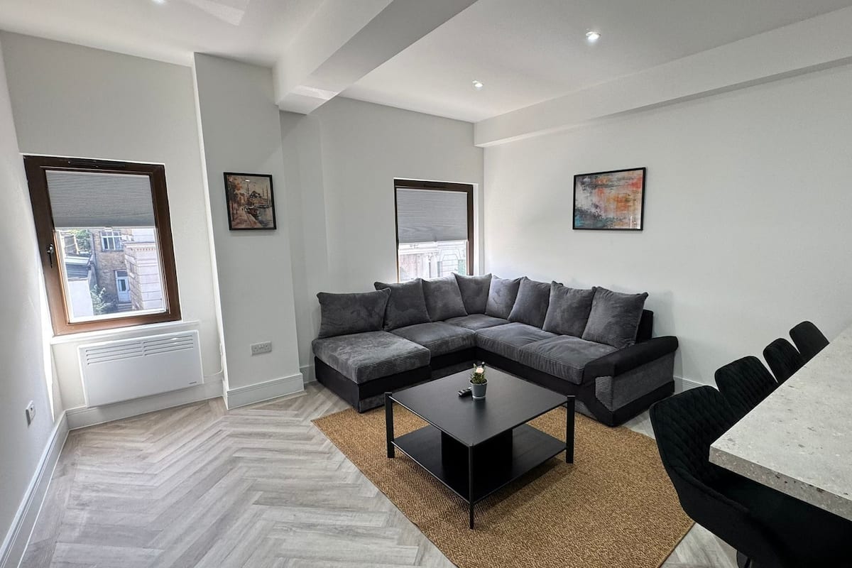A modern living room with a sectional sofa, a coffee table, a dining table with chairs, and artwork on the walls.