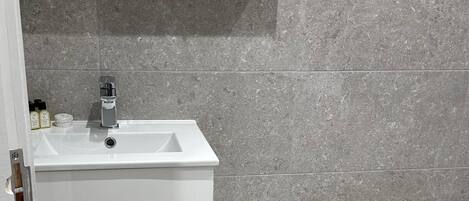 Un baño con un lavabo blanco, un espejo y un cubo de basura negro.