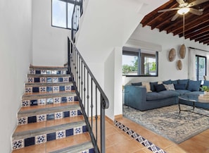 Un escalier orné de carreaux décoratifs, un canapé bleu et un ventilateur de plafond dans un salon.