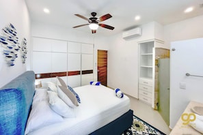 A modern hotel room with a large bed, a ceiling fan, a wardrobe, and a bathroom with a sink and mirror.