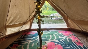 Interior de uma tenda com chão estampado em flor, uma videira decorativa com luzes e vista para uma área gramada lá fora.