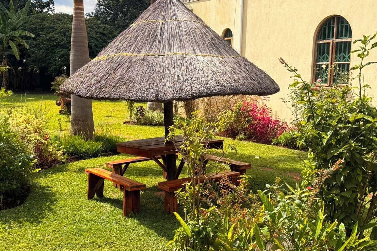 A thatched-roof gazebo with picnic tables in a well-maintained garden.