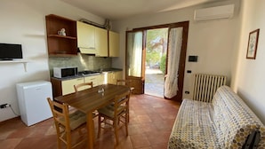 Una cocina compacta con una mesa de comedor y sillas, un refrigerador pequeño y un sofá con un cubre sábana estampado.