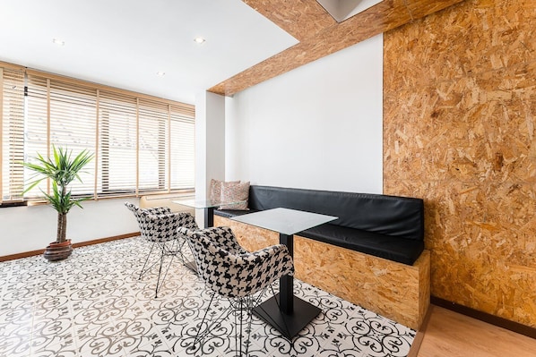 A modern lounge area with a black sofa, patterned chairs, a glass table, and a potted plant. - Guestready Economy - Portfolio Guesthouse (Porto)