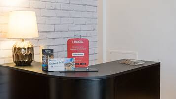 A reception desk with a lamp, a LUGGIt luggage delivery sign, a Welcome to Porto sign, and a promotional card.