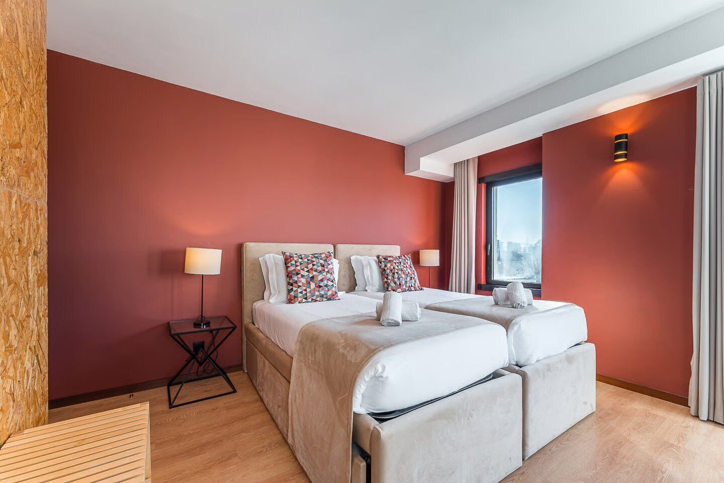 Moderni hotellihuone, jossa on suuri sänky, kaksi yöpöytää ja ikkuna, jossa on verhot.