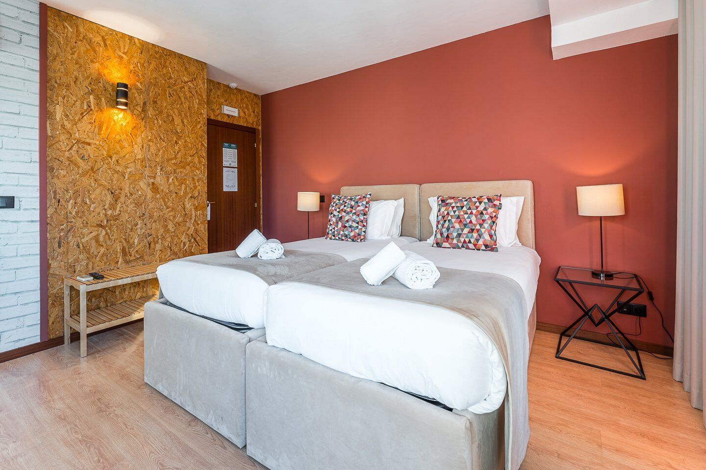 A double bed with two pillows, a bedside table, a lamp, and a wall with a textured pattern.