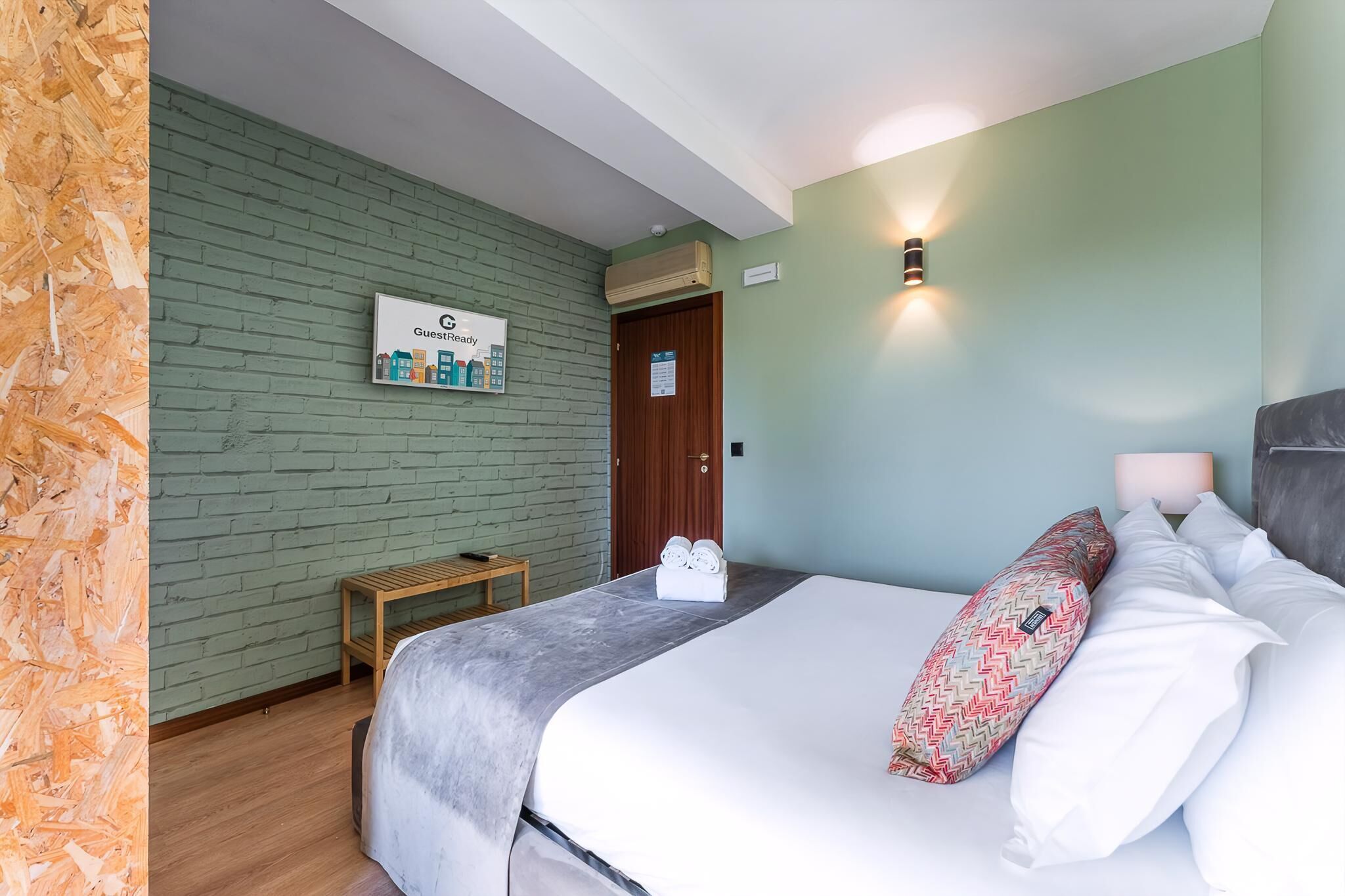 Una habitación de hotel con una cama, una mesita de noche de madera, un cartel en la pared y una puerta.