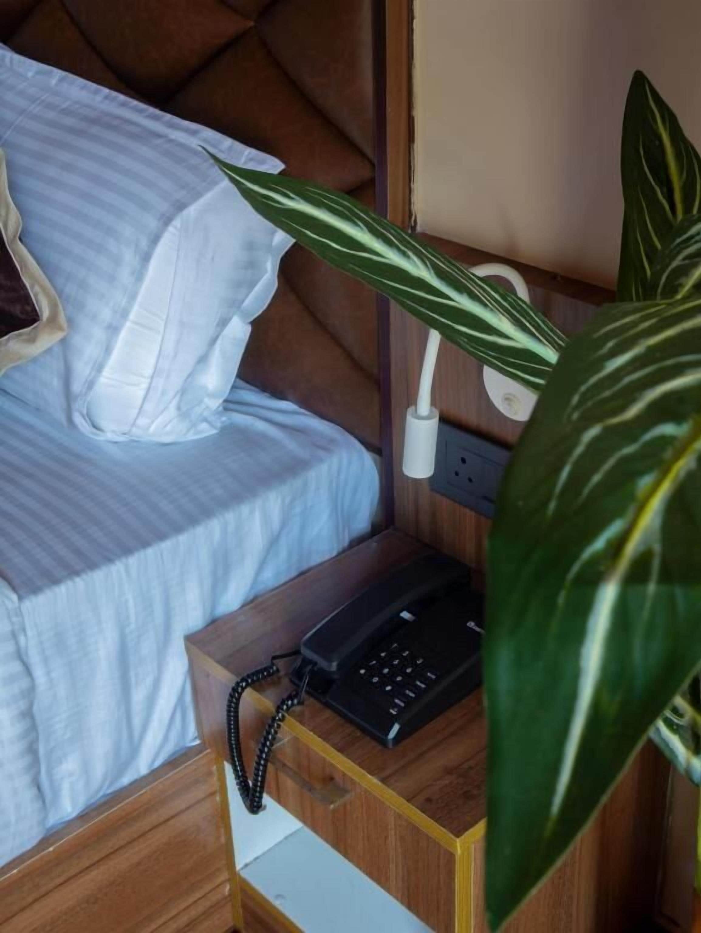 A neatly made bed with white linens, a bedside telephone, and a wooden nightstand.
