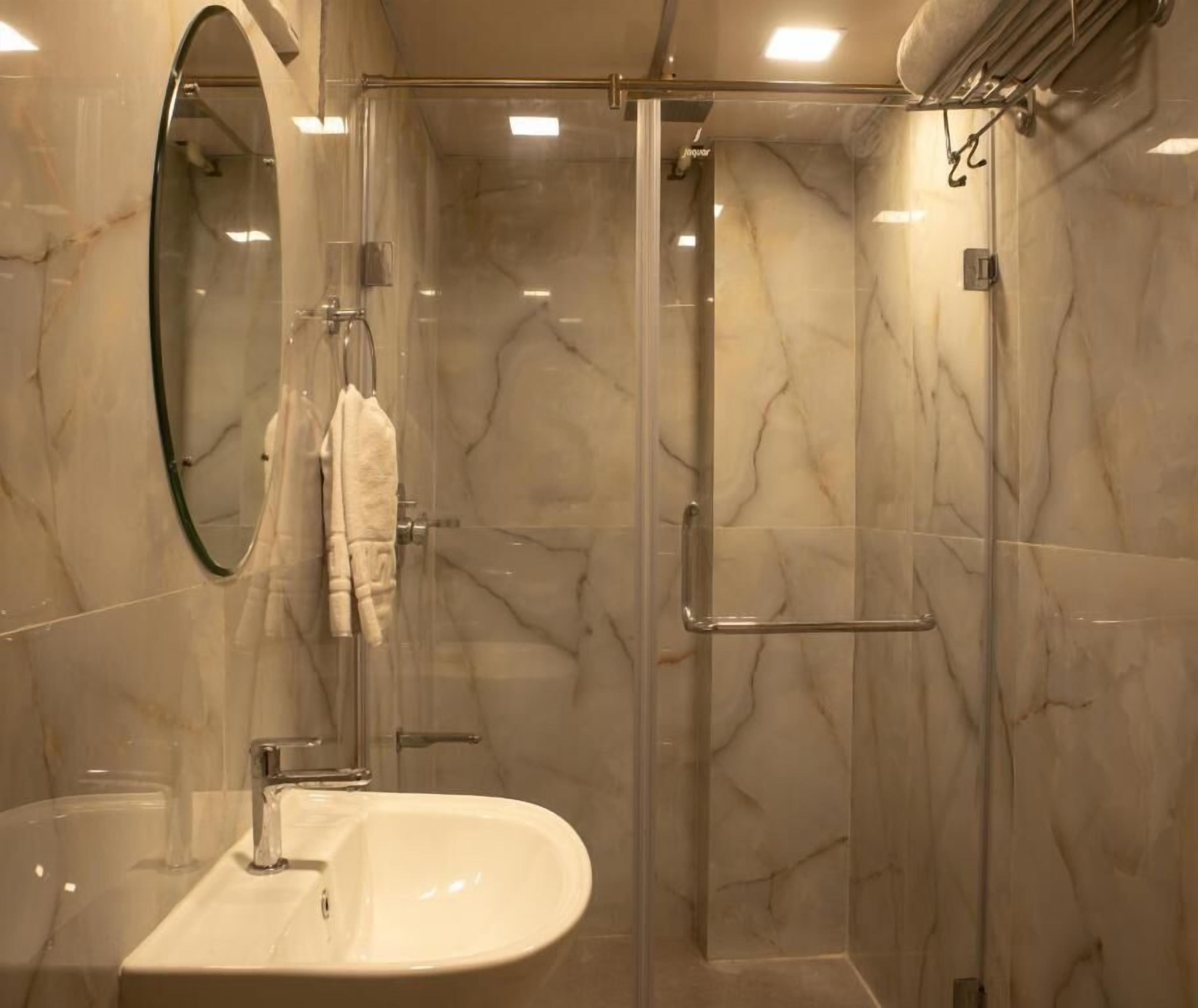 A modern bathroom with a glass-enclosed shower, a marble-tiled wall, and a white sink.