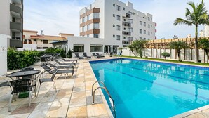 Una piscina con sillones de descanso y un borde de baldosas, rodeada de edificios y vegetación.
