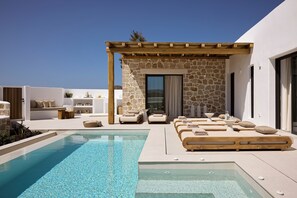 A modern outdoor pool area with lounge chairs and a stone wall. - Villa Aethera Milos (Milos)