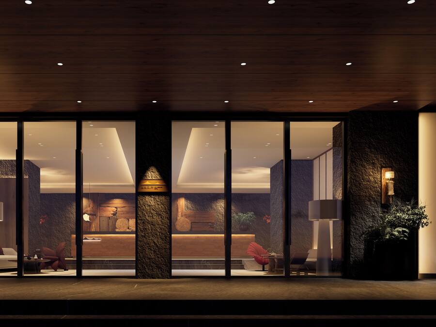 Un moderno vestíbulo de hotel con una columna de piedra, techo de madera y grandes puertas de vidrio que dan al interior.