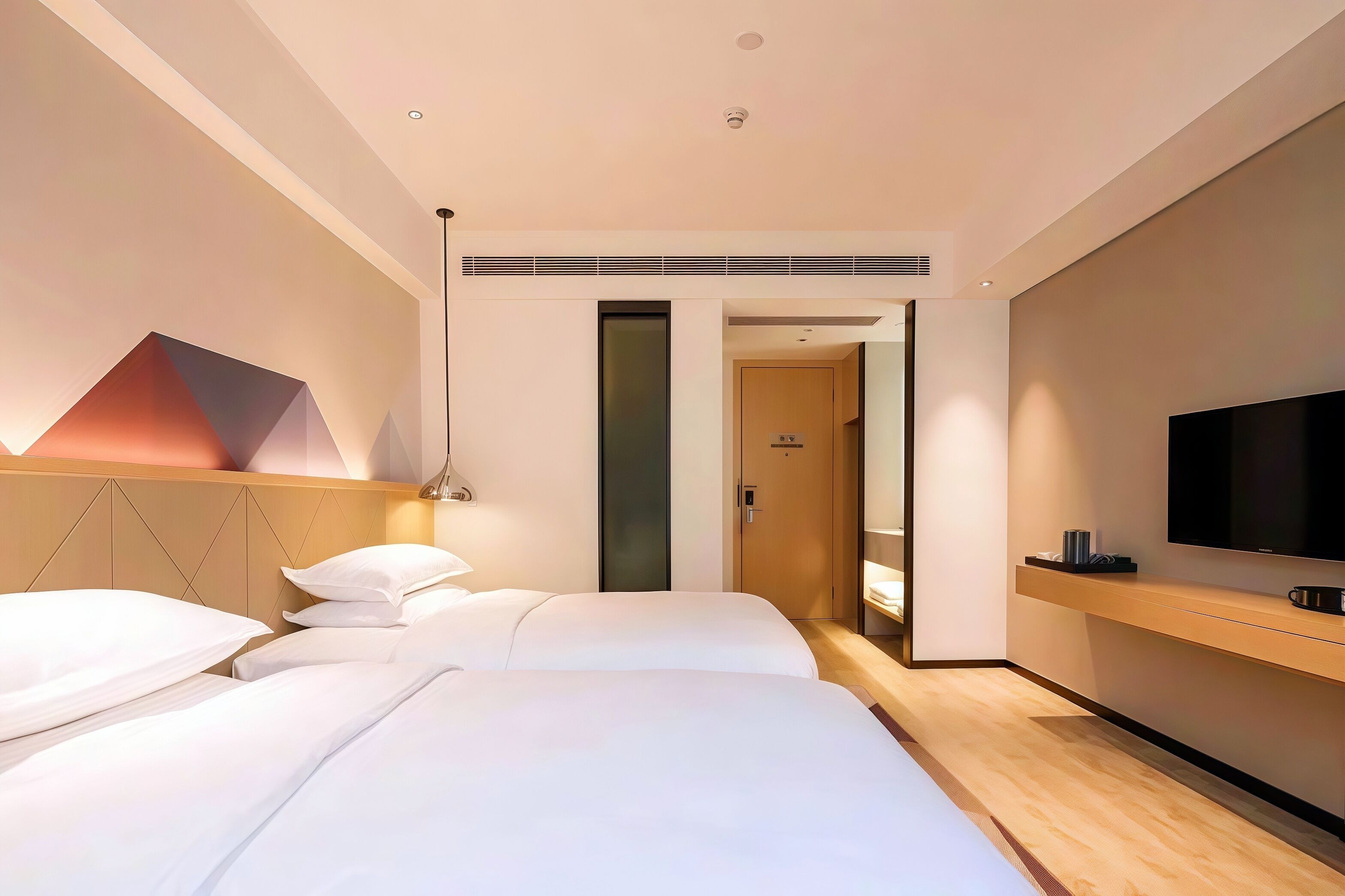 A modern hotel room with two beds, a TV, and a wooden bedside table.