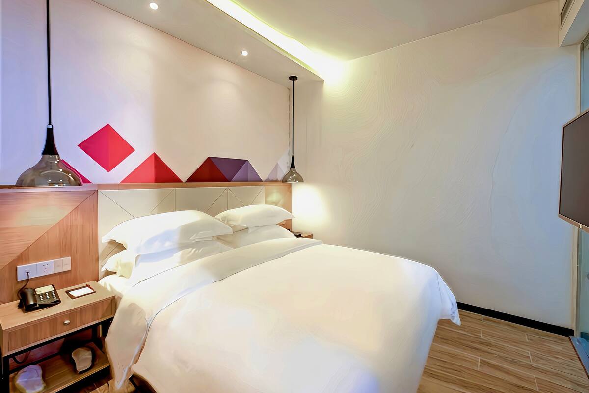 A hotel room with a bed, bedside table, lamp, and a wall with geometric patterns.