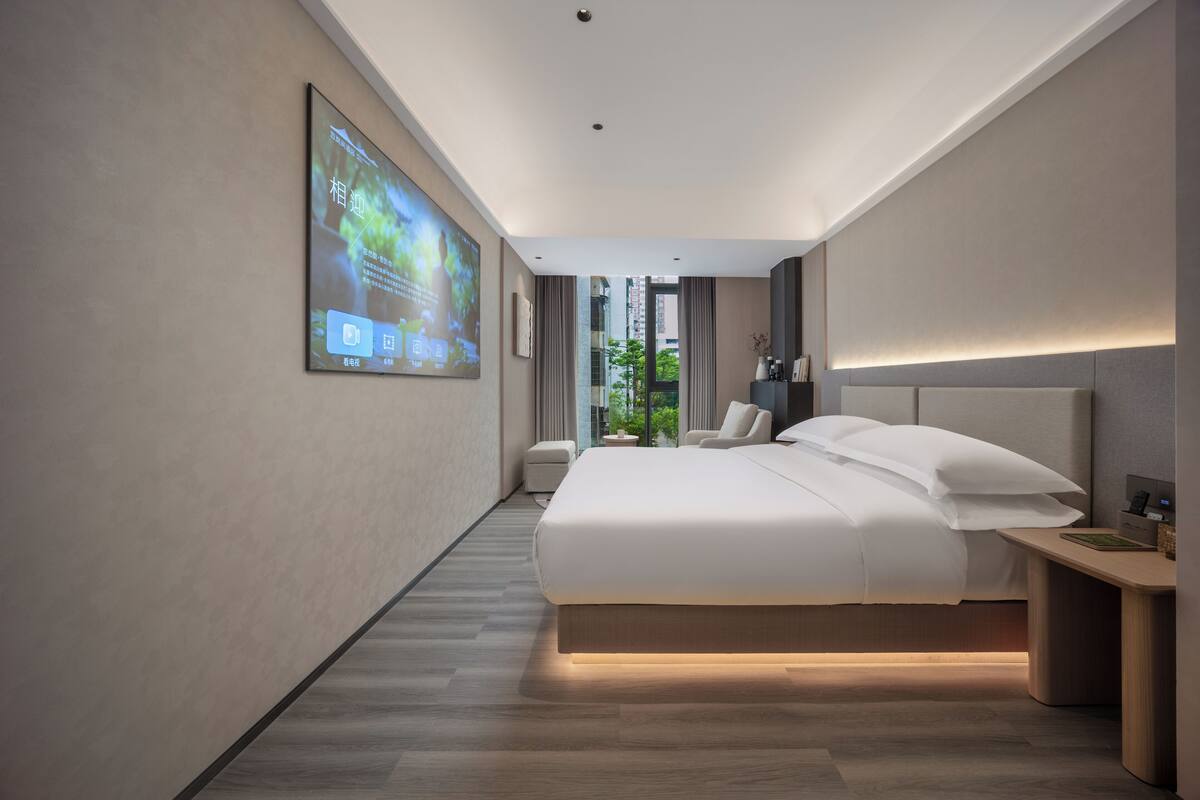 A modern hotel room with a large bed, a desk, and a large screen displaying content.