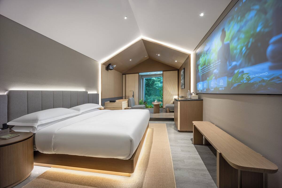 A modern bedroom with a large bed, bedside tables, a bench, and a projection screen displaying a nature scene.