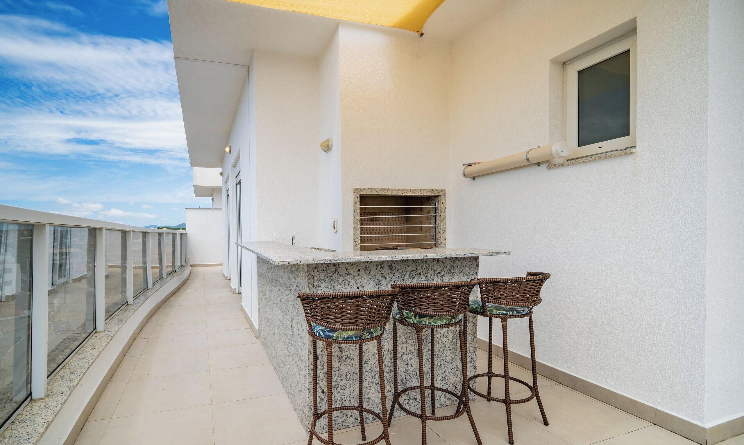 A balcony with a bar area, two wicker chairs, a window, and a view of the sky.
