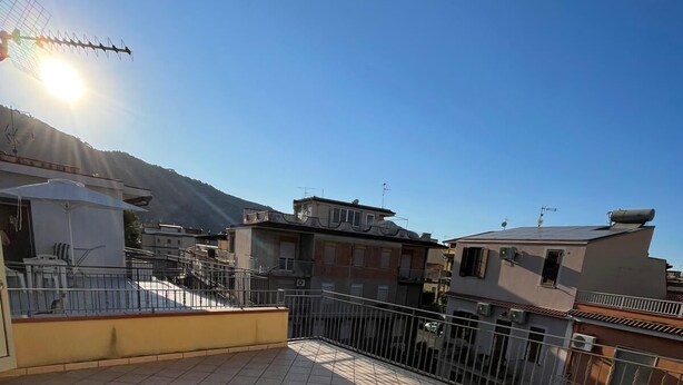 A rooftop terrace with tiled flooring, a metal railing, and a view of surrounding buildings and a mountain. - Comfortable and quiet house near the sea (Oliveri)