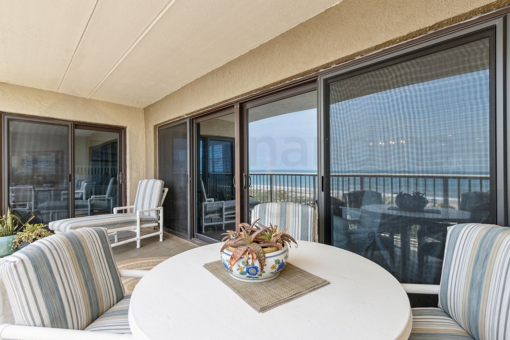Een balkon met een ronde tafel, gestreepte stoelen en een bloempot.