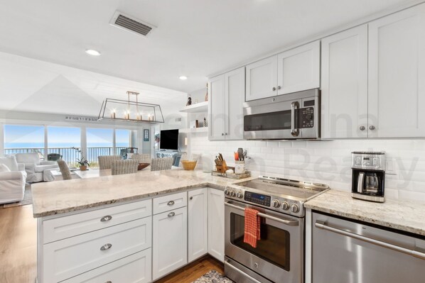 Una cocina moderna con armarios blancos, electrodomésticos de acero inoxidable y un amplio ventanal con vistas al mar.