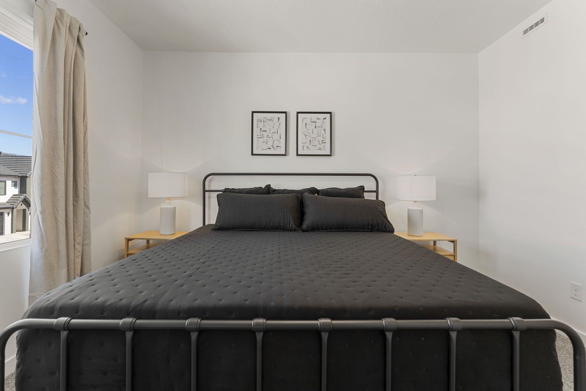 Een slaapkamer met een zwart bed, twee bedlampen en twee afbeeldingen in een lijst aan de muur.