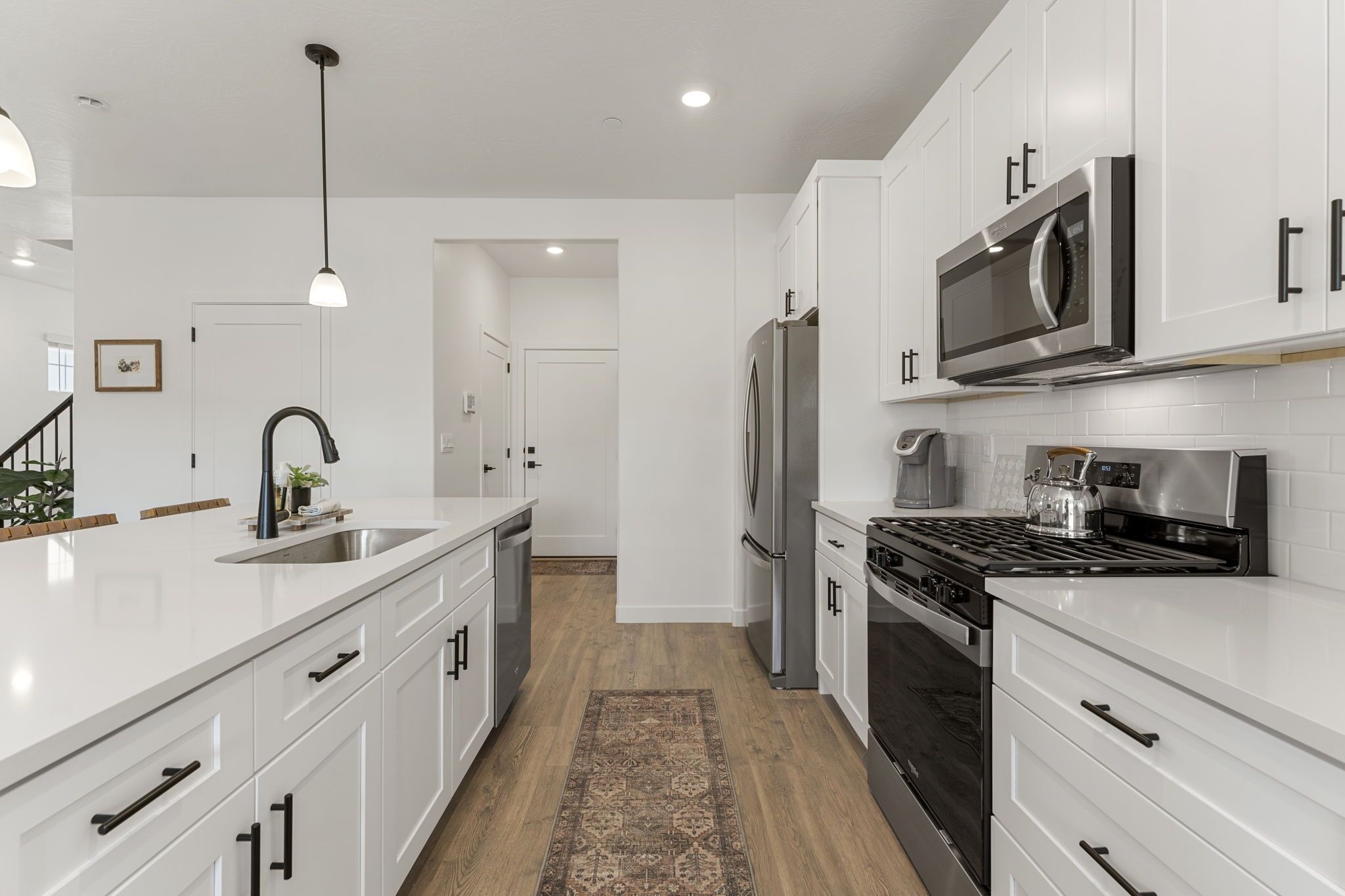 A modern kitchen with white cabinetry, stainless steel appliances, and a wooden floor.