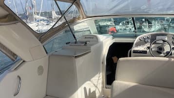 Interior de una embarcación con timón, panel de control y vista de otras lanchas en un puerto deportivo.