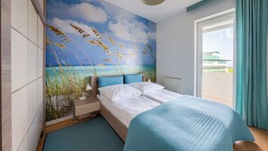 Une chambre à coucher avec un lit, une table de chevet, une lampe et une vue sur la mer par la fenêtre.