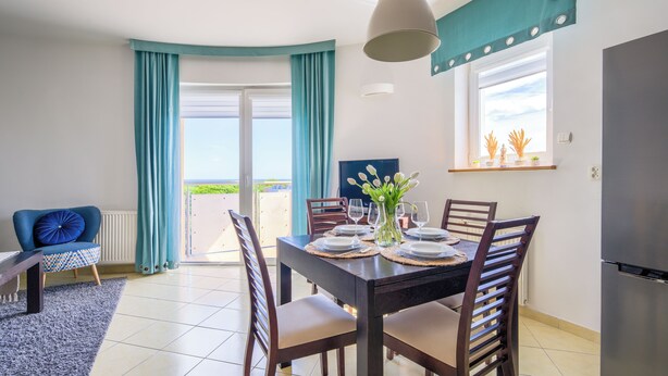 Un coin repas avec une table dressée pour quatre personnes, des chaises, un vase rempli de fleurs et une vue sur l’extérieur grâce à une porte coulissante.