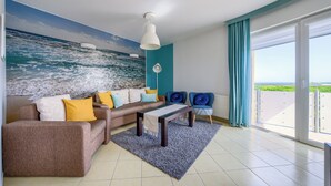 Un salon moderne avec une grande fresque représentant l’océan, un ensemble de canapés, une table basse et une vue sur la mer grâce à une porte-fenêtre coulissante.