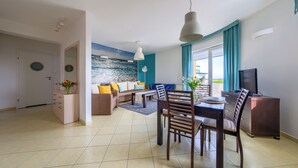 Un salon moderne avec un canapé, une table à manger et des chaises. On y trouve également un téléviseur et une fenêtre avec des rideaux.