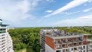 Un immeuble à plusieurs étages doté d’une terrasse sur le toit, entouré d’une végétation luxuriante et surplombant un ciel dégagé.