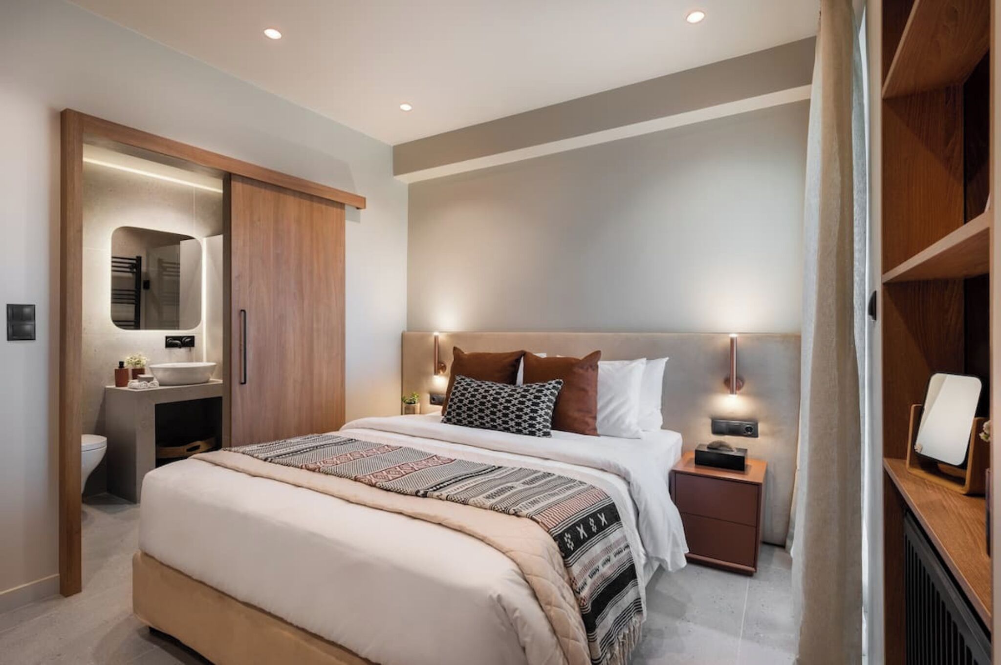 A modern bedroom with a large bed, bedside tables, a built-in wardrobe, and a mirror.