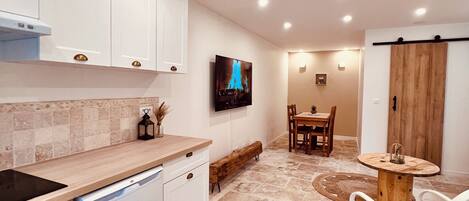 A modern kitchen with white cabinets, a built-in oven, and a dishwasher. There is a dining area with a wooden table and chairs.