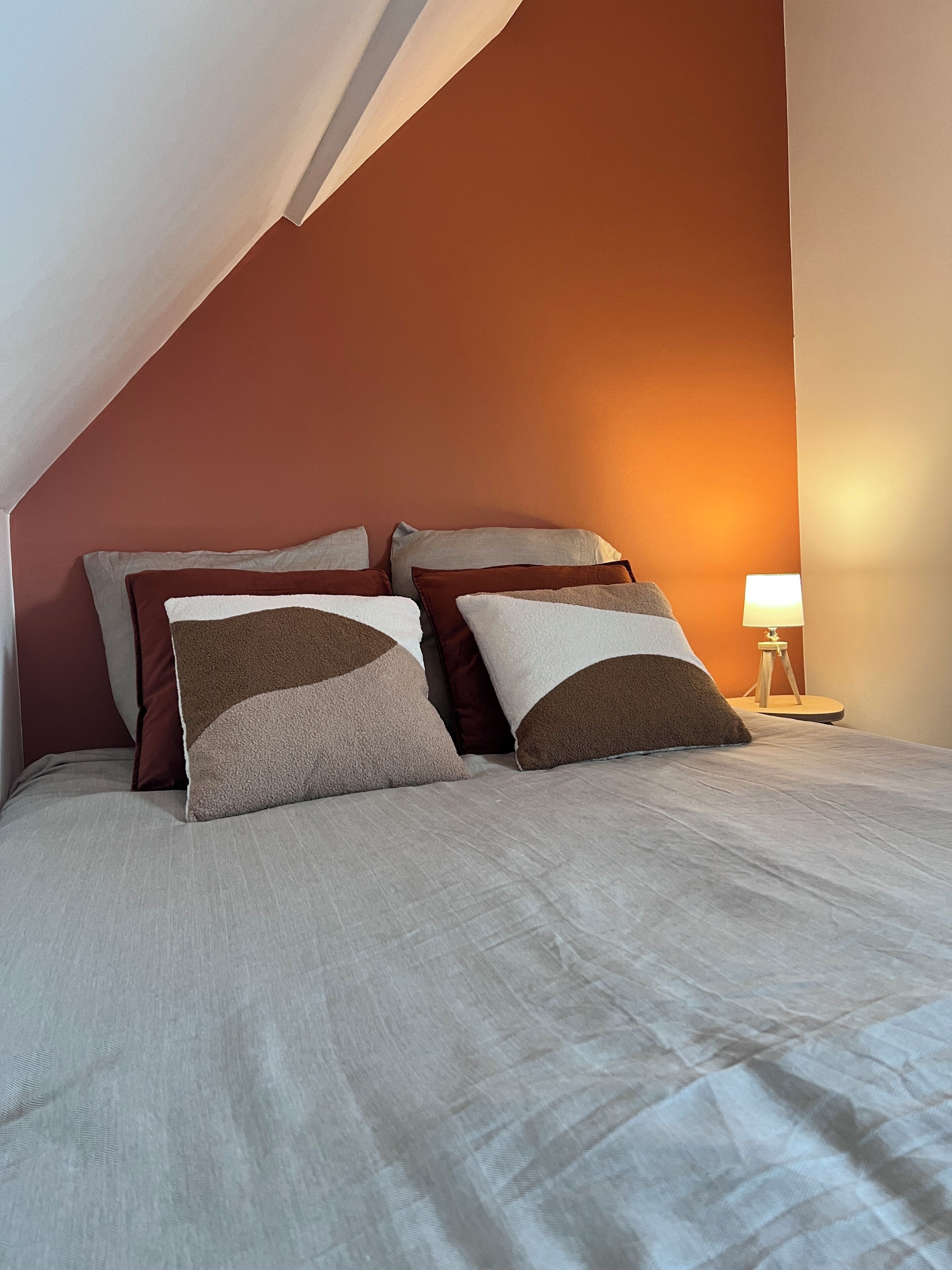 A neatly made bed with a white duvet and several pillows in shades of brown and beige.