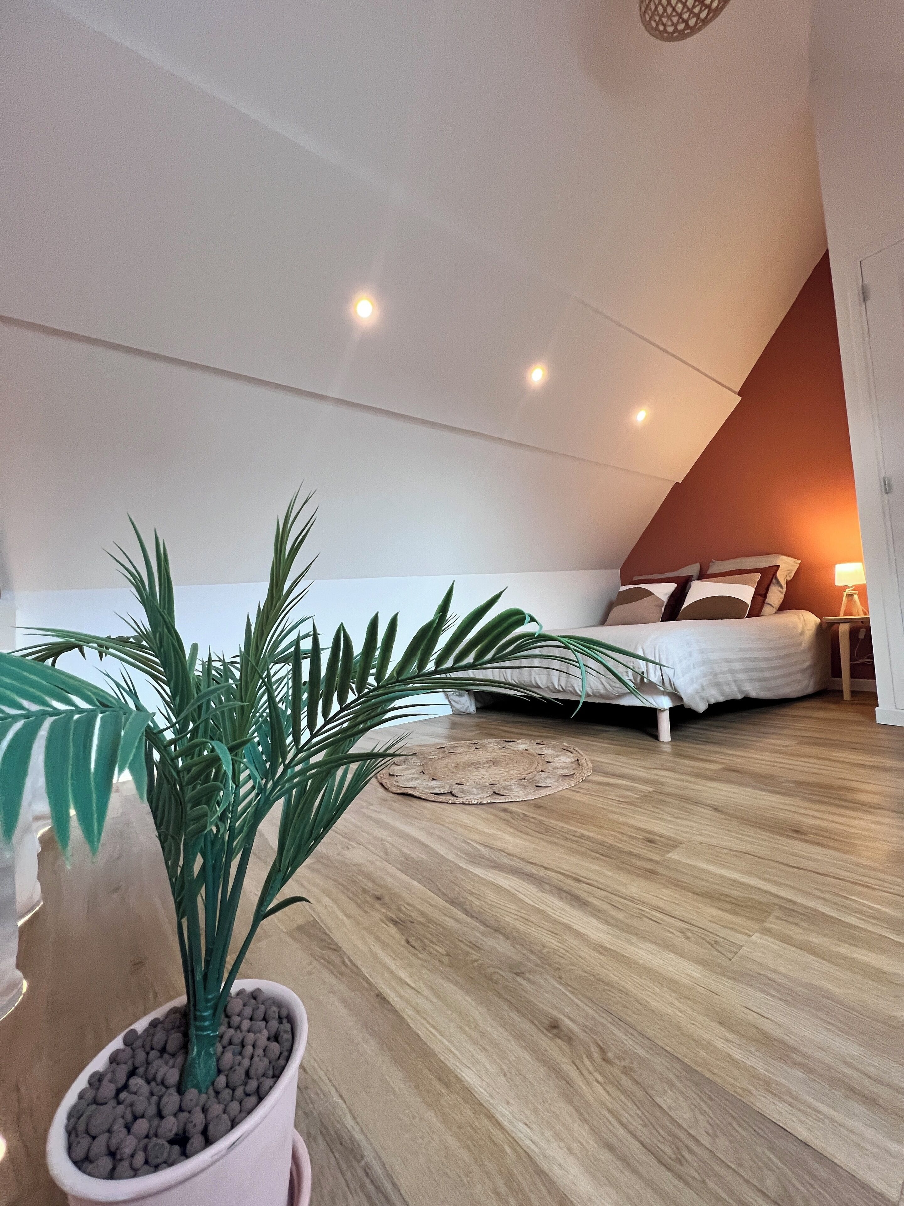 Un dormitorio con techo inclinado, una cama con almohadas, una mesita de noche con lámpara y una planta en maceta.