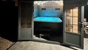 A small, enclosed outdoor space with a hot tub, a bench, and a door leading to the outside.