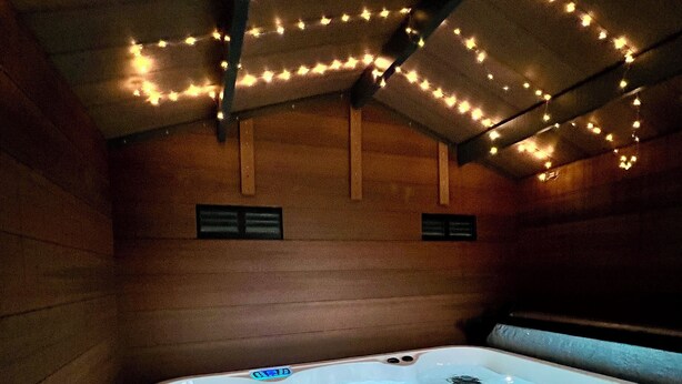 A hot tub with a wooden interior, string lights, and a visible control panel.