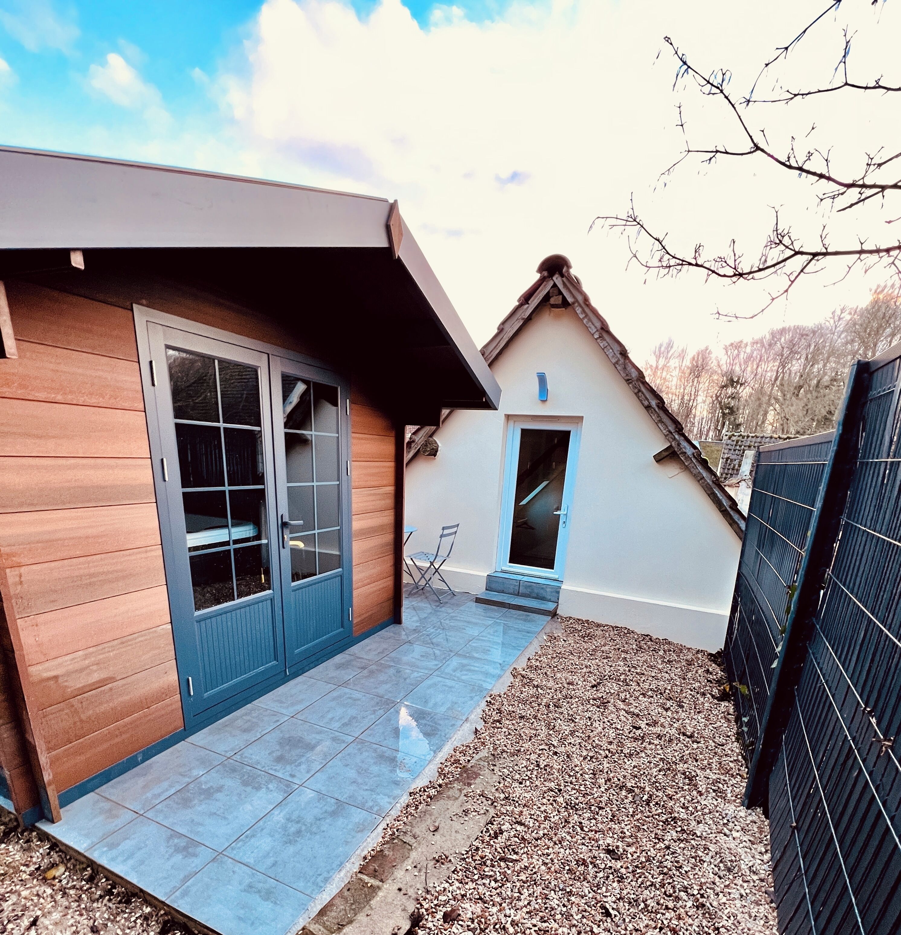 Une maison moderne avec une façade en bois, une porte bleue et une terrasse carrelée.