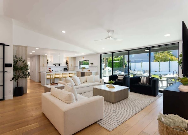 A modern living room with a sofa, coffee table, and a view of the kitchen and outdoor area.
