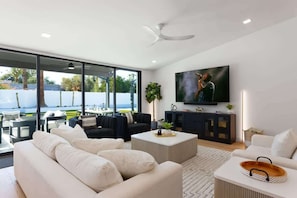 A modern living room with a large TV, comfortable seating, and a view of the outdoors.