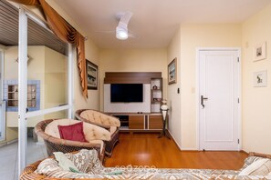 A living room with a television, a sofa, a wicker chair, and a door. - Apt With Grill 300m From the Beach Mdo201 (Florianópolis)