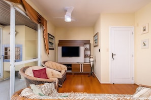 Una sala de estar con televisor, sofá, sillón de mimbre y una puerta.